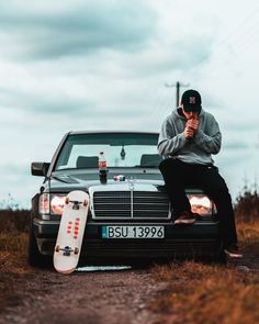 a man sitting on the hood of a car holding a skateboard