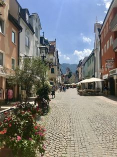 a cobblestone street lined with shops and people walking down one side in the distance