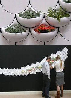 two people standing next to each other in front of a wall with planters on it