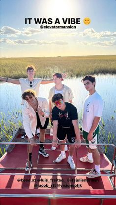 four young men standing on top of a boat in front of a body of water