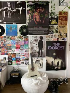 a guitar sitting on top of a white bean bag in front of a wall covered with posters