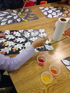 children are sitting at a table painting with watercolors on paper and paintbrushes