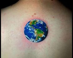 a small earth tattoo on the back of a woman's shoulder, with blue and green paint