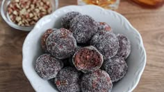 a white bowl filled with powdered sugar covered doughnuts next to two glasses