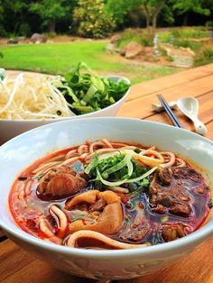 two bowls of food sitting on top of a wooden table next to a bowl of noodles