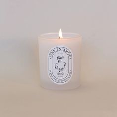 a white candle with a label on it sitting in front of a gray background,