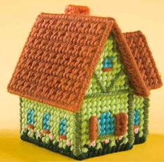 a crocheted house is shown on a yellow tablecloth with a brown roof