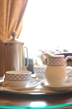 a plate with cups and saucers sitting on top of it next to a coffee pot