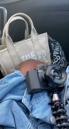 a camera and some other items sitting in the back seat of a car, including a tote bag