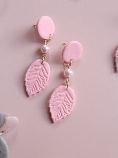 two pink earrings with leaves and pearls hanging from them on a pink surface next to flowers