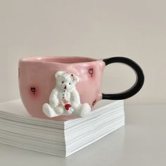 a pink coffee cup with a white teddy bear on it sitting next to stack of cards