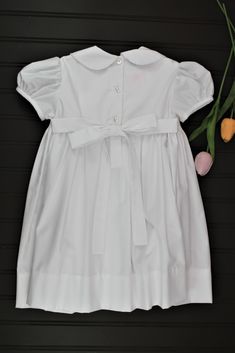 This classic dress is perfect for weddings, christenings, or blessings. The smocking on the bodice is accented with white pearls. 65% Polyester - 35% Cotton Machine wash 3 Button back closure Fitted Smock Wedding Dress, Fitted Wedding Dress With Smocked Cuffs, Elegant Baptism Dress With Smocked Back, Elegant Smocked Dress With Smocked Cuffs For Baptism, Elegant Dress With Smocked Back For Baptism, Elegant Fitted Smock Dress, Elegant Smocked Ruffle Dress For Baptism, Elegant Smocked Dresses For Baptism, Elegant Smock Dresses For Baptism