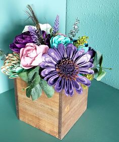 an arrangement of flowers in a wooden box on a green table next to a blue wall