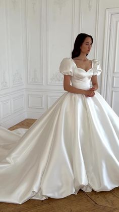 a woman in a white wedding dress standing on the floor with her hands behind her back