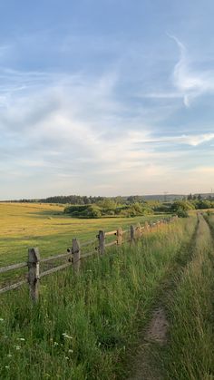 a grassy field with a wooden fence in the foreground and an empty road on the other side