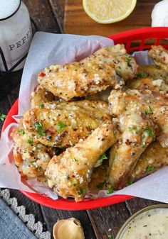 baked chicken wings in a red basket with garlic and parsley on the side next to a bowl of ranch dressing