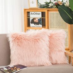 two pink fluffy pillows on a couch in front of a book shelf and planter