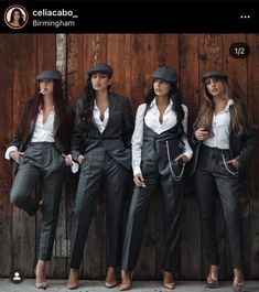 three beautiful women standing next to each other in front of a wooden wall wearing suits and hats