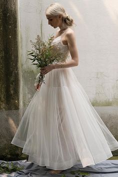 a woman in a white wedding dress holding a flower bouquet and looking down at the ground