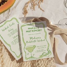 two wedding cards sitting on top of a table next to a glass of watermelon