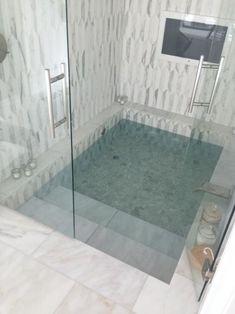 a glass enclosed shower stall in a white tiled bathroom with marble walls and flooring