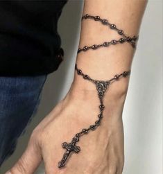 a person wearing a rosary bracelet with a cross tattoo on their left wrist and the other hand