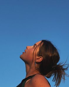 a woman looking up into the sky with her hair blowing in the wind while flying a kite