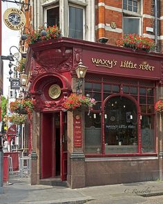 a red store front with flower boxes on the windows and flowers hanging from it's sides