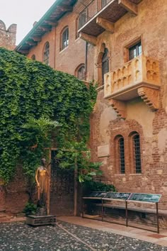 an old brick building with ivy growing on it's sides and a statue in the courtyard