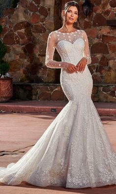 a woman in a white wedding dress standing on a stone patio with her arms behind her back