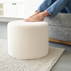 a person sitting on top of a white ottoman with their feet resting on the ottoman