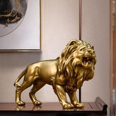 a golden lion statue sitting on top of a wooden table next to a framed painting