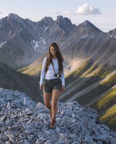 a beautiful young woman standing on top of a mountain