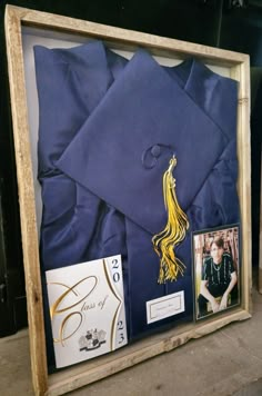 a graduation cap and gown are displayed in a wooden frame with other items around it