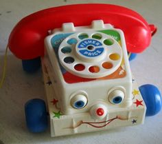 an old fashioned toy phone sitting on top of a white table with blue and red wheels