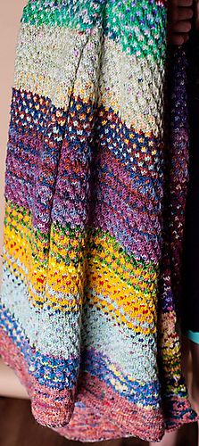 a woman is holding up a colorful crocheted blanket