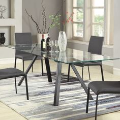 a glass dining table with grey chairs in front of a white and gray area rug