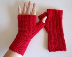 a woman's hand wearing red knitted fingerless gloves on top of a white surface