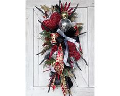 a red and black christmas wreath hanging on a white door with silver ornaments around it