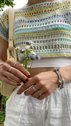 a woman holding flowers in her hand while wearing rings and a crochet top