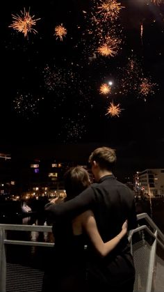 two people standing next to each other with fireworks in the sky