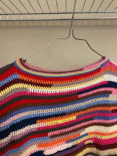 a multicolored crocheted sweater hanging on a metal rack with clothes pins