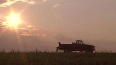 a pickup truck is parked in a field with the sun setting behind it and two people sitting in the back