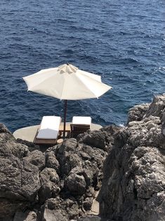 two chairs and an umbrella on the rocks by the water