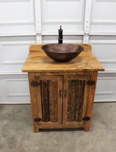 a wooden cabinet with a metal bowl on top and a bottle in the corner next to it