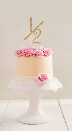 a white cake with pink flowers and a gold number twenty one on top is sitting on a pedestal