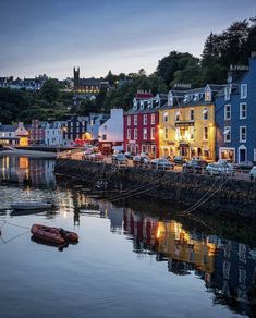 the boats are docked in the water by the buildings on the shore at night time