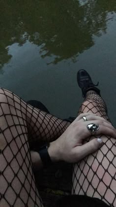 a person wearing fishnet stockings sitting on the ground next to a body of water