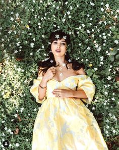 a woman wearing a yellow dress standing in front of green plants and white daisies