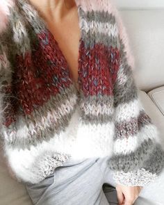 a woman sitting on top of a white couch wearing a red and grey knitted sweater